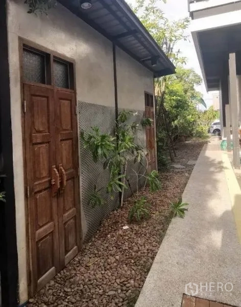 Detached House for sale in Pak Kret, Nonthaburi - Side walkway with pebble landscaping and rustic wooden doors beside the house.
