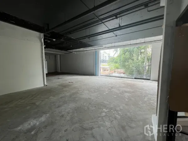 Retail Space for rent - Open-plan retail floor featuring exposed services and a large glass frontage facing greenery.