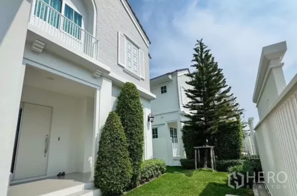 Detached House for rent in Bang Phli, Samut Prakan - Front lawn with manicured shrubs and tall evergreen beside the facade.