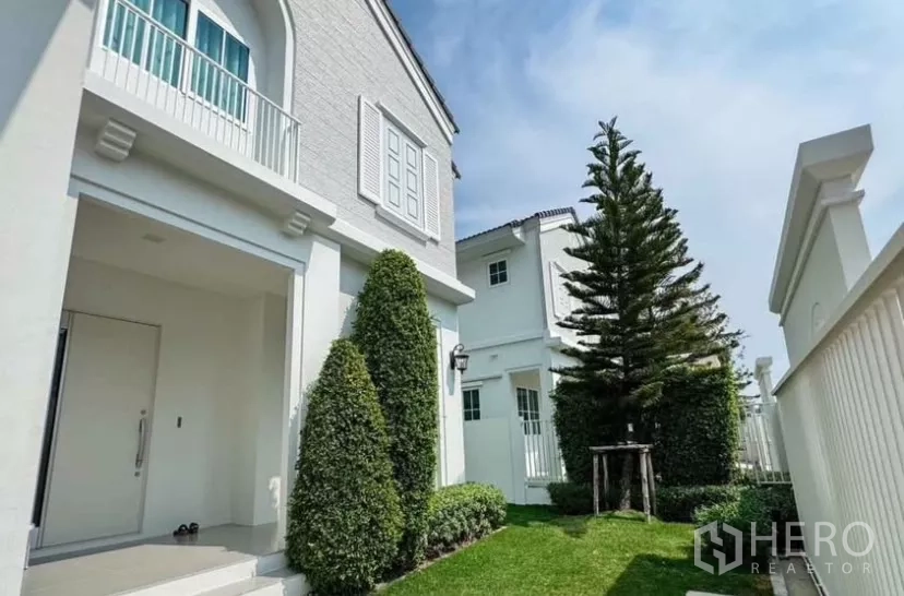 Detached House for rent in Bang Phli, Samut Prakan - Front lawn with manicured shrubs and tall evergreen beside the facade.