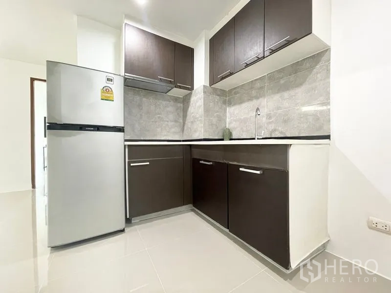 Condominium for rent in Khlong Toei, Bangkok - Compact kitchen with dark cabinetry, tiled backsplash, and a refrigerator.
