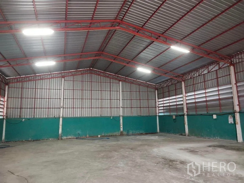 Warehouse for sale in Lam Luk Ka, Pathum Thani - Spacious warehouse interior with high red steel trusses and bright lighting.