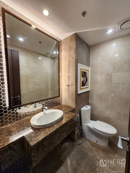 Condominium for rent in Khlong Toei, Bangkok - Guest bathroom with marble vanity, large mirror and modern toilet.