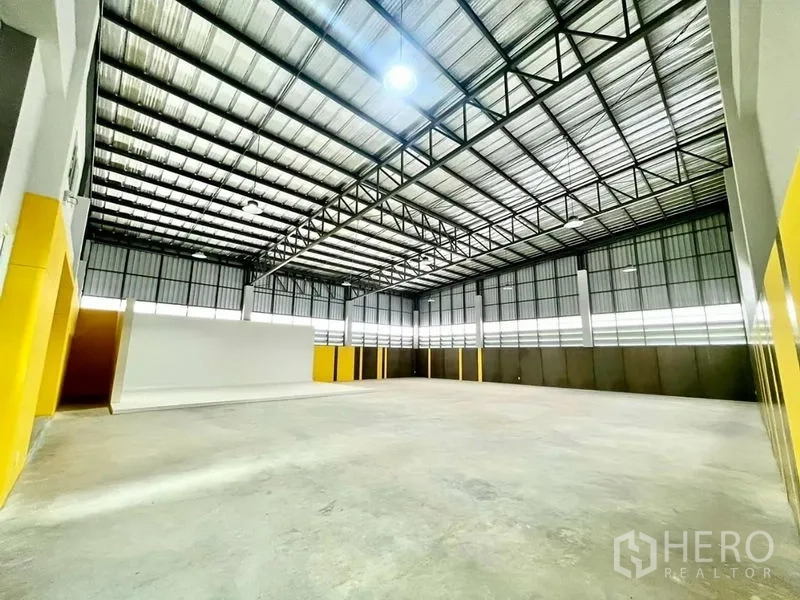 Warehouse for sale in Lam Luk Ka, Pathum Thani - Open factory floor with polished concrete, skylight panels and yellow accent walls along the perimeter.