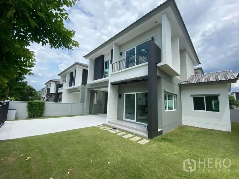 Detached House for rent in Khlong Luang, Pathum Thani - Side view showing green lawn, small patio and large glass doors to the garden.
