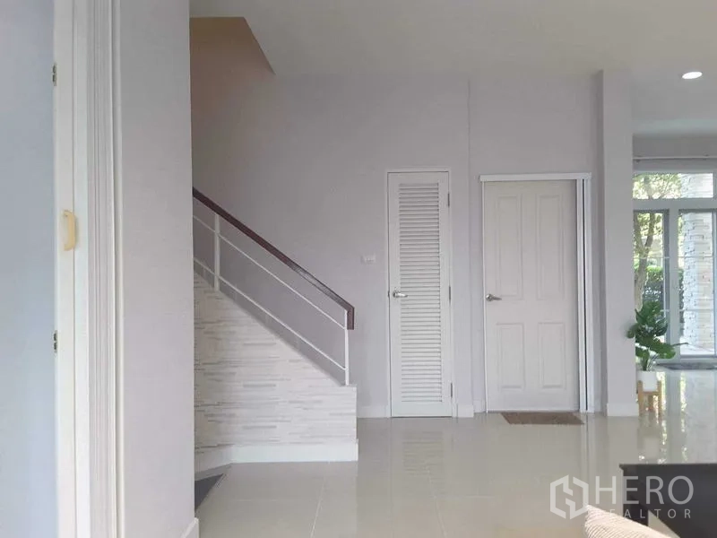 Detached House for rent in Lam Luk Ka, Pathum Thani - Hallway with white staircase railing and two storage doors in a clean minimalist style.