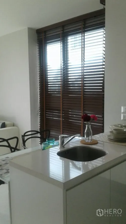 Condominium for rent in Khlong Toei, Bangkok - Compact kitchenette with white island sink, vase and wooden Venetian blinds.