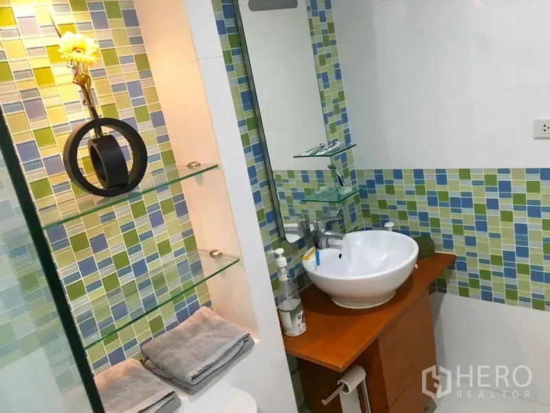 Condominium for rent in Pathum Wan, Bangkok - Bathroom vanity with round vessel sink, wooden cabinet, and glass shelving with green-blue mosaic tiles.