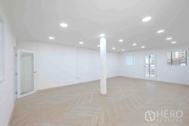 Standalone for rent or sale in Bang Na, Bangkok - Renovated office room with wood-look herringbone floor and recessed lighting.