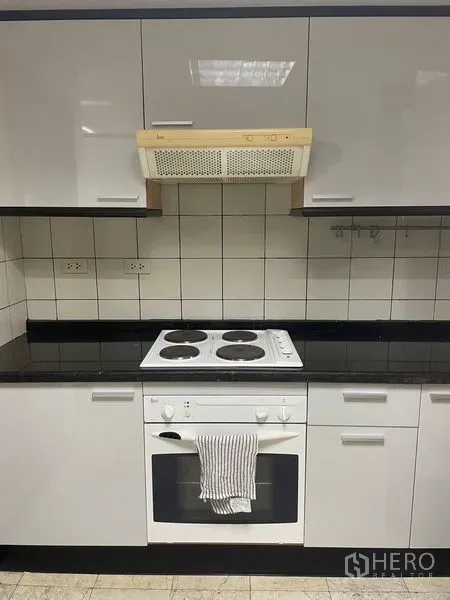 Condominium for rent in Pathum Wan, Bangkok - Kitchen cooking zone with electric cooktop, oven, tiled backsplash and range hood.