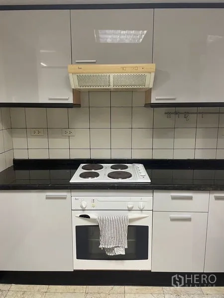 Condominium for rent in Pathum Wan, Bangkok - Kitchen cooking zone with electric cooktop, oven, tiled backsplash and range hood.