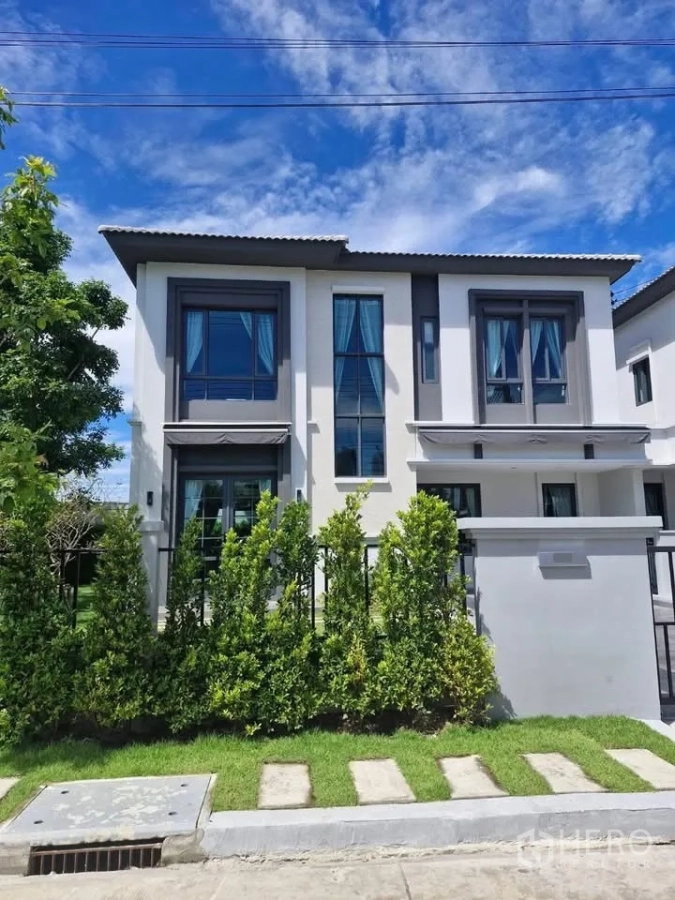 Detached House for rent in Bang Phli, Samut Prakan - Modern two-storey detached house facade with tall windows and front hedge under blue sky.