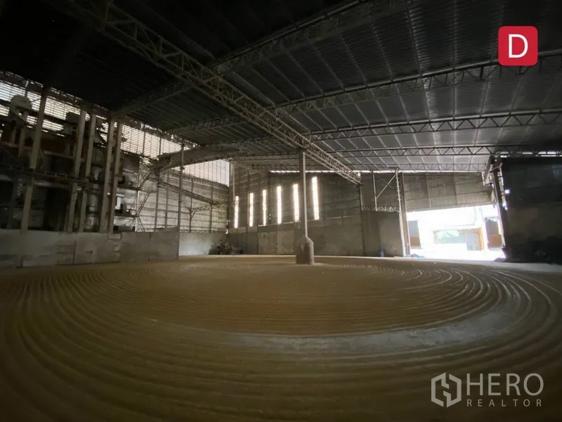 Factory for rent in Chachoengsao - Spacious factory interior with steel truss roof, circular textured floor and natural light panels.