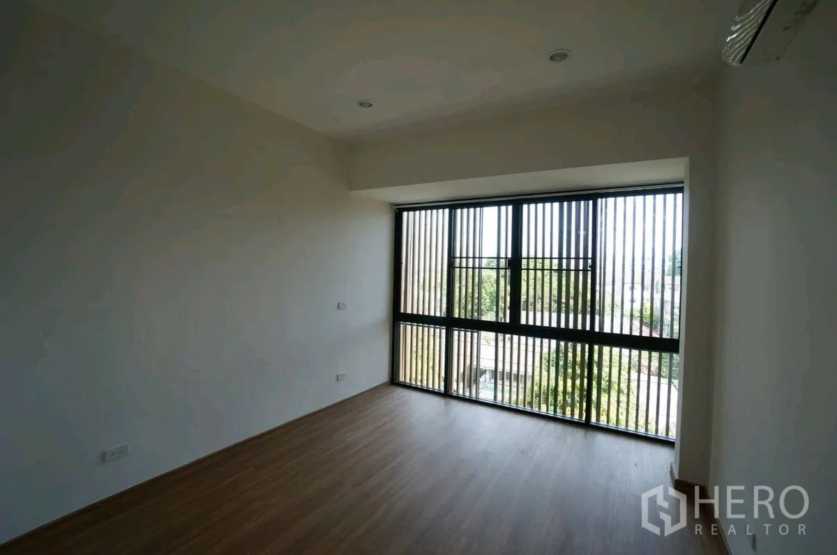 Home Office for rent in Chatuchak, Bangkok - Empty room with wood flooring and a large window with vertical slat screen.