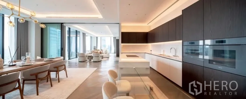 Condominium for rent or sale in Pathum Wan, Bangkok - Open-plan gourmet kitchen with marble island, dark wood cabinetry and a dining area beside floor-to-ceiling windows with city views.