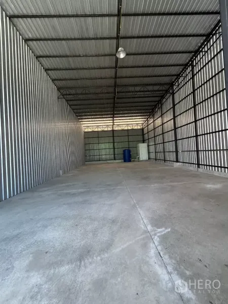 Warehouse for rent in Ban Pho, Chachoengsao - Interior of the warehouse showing high steel-truss roof, lighting, and open concrete space for storage.