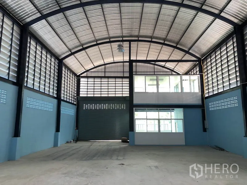 Factory for rent or sale in Bang Bua Thong, Nonthaburi - Warehouse interior facing a wide roller shutter and two-level office block.