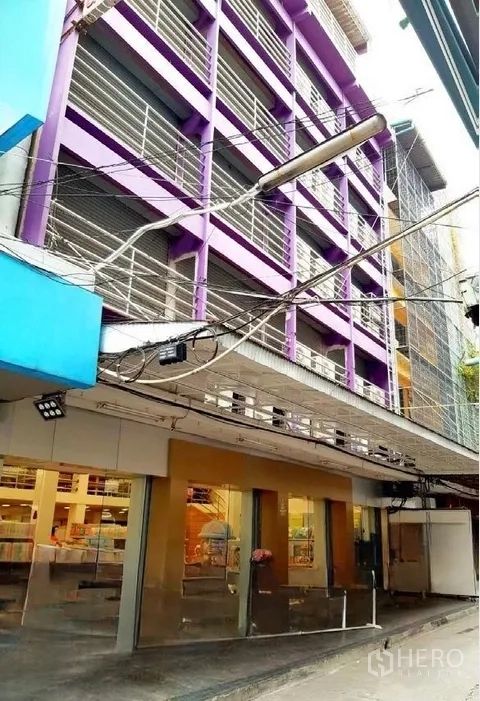 Shophouse for rent in Pathum Wan, Bangkok - Angled street view of the same purple shophouse with glass retail frontage and overhead signage along a narrow lane.