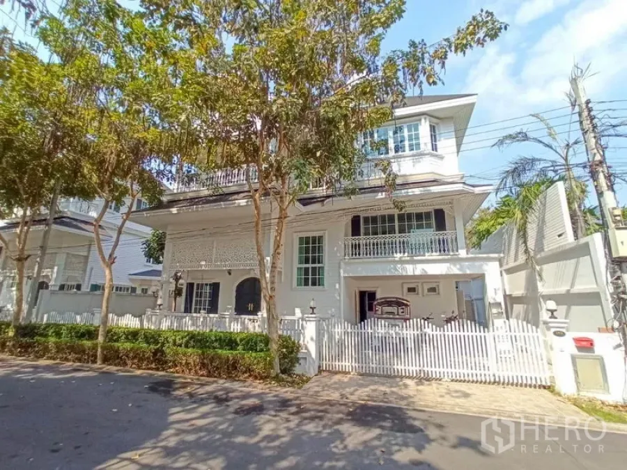 Detached House for rent in Mueang Samut Prakan, Samut Prakan - White detached house exterior with balconies, picket fence and mature trees on a quiet Samut Prakan street.