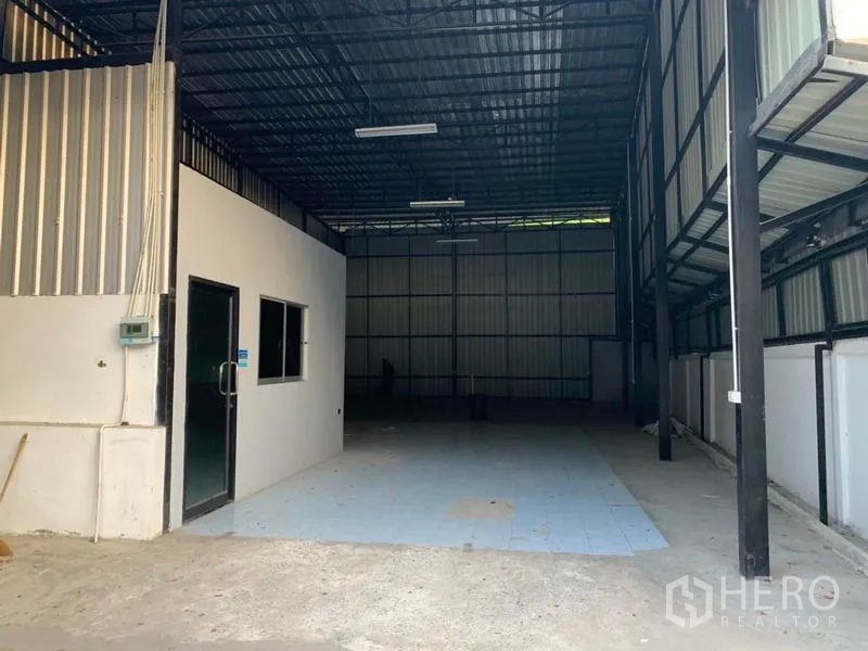 Warehouse for rent in Bang Kapi, Bangkok - Spacious warehouse interior showing high ceiling, steel frames, concrete floor and a small office unit.