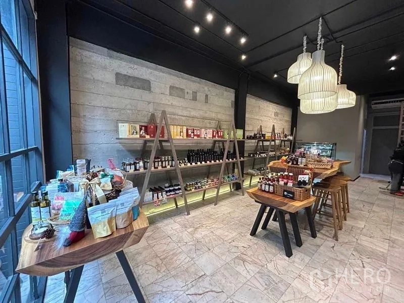 Retail Space for rent in Bang Rak, Bangkok - Modern retail space featuring concrete accent wall, track lighting, wood tables and window-side shelving.