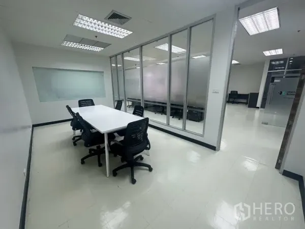 Office Space for rent - Compact meeting room with a white table and office chairs beside a floor-to-ceiling glass partition.