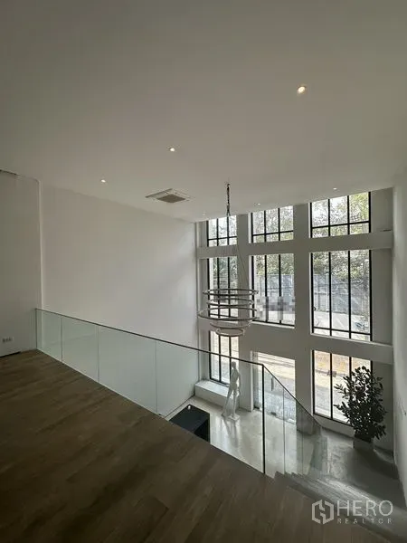 Home Office for rent in Phra Khanong, Bangkok - Mezzanine workspace with glass balustrade overlooking floor-to-ceiling windows and chandelier.
