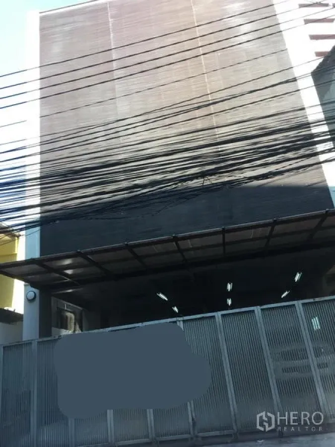 Home Office for rent in Watthana, Bangkok - Multi-storey home office building with metal gate, covered entrance canopy, and overhead power lines on an urban lane.