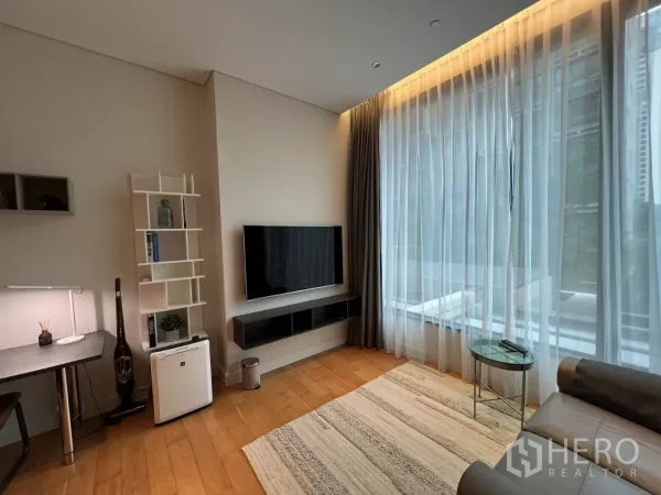 Condominium for rent in Pathum Wan, Bangkok - TV wall and work desk facing sheer floor-to-ceiling curtains in a cozy living space.