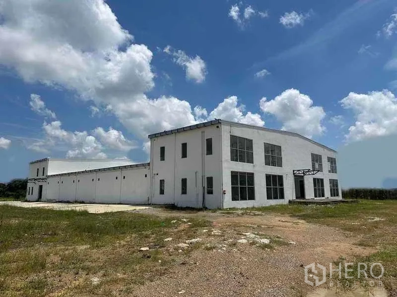 Warehouse for rent in Sai Noi, Nonthaburi - Front facade of modern white warehouse with large windows and open yard area.
