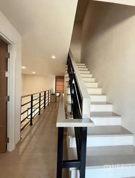 Townhouse for rent in Bang Phli, Samut Prakan - Staircase with black metal railing leading to a mezzanine hallway in the townhouse.
