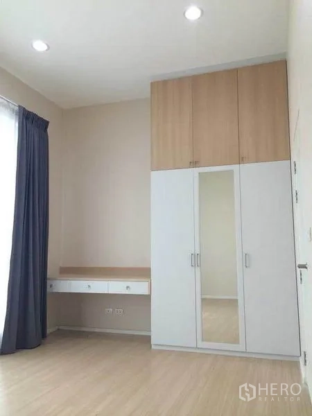 Townhouse for sale in Suan Luang, Bangkok - Bedroom with tall built-in wardrobe, study desk and curtained window.
