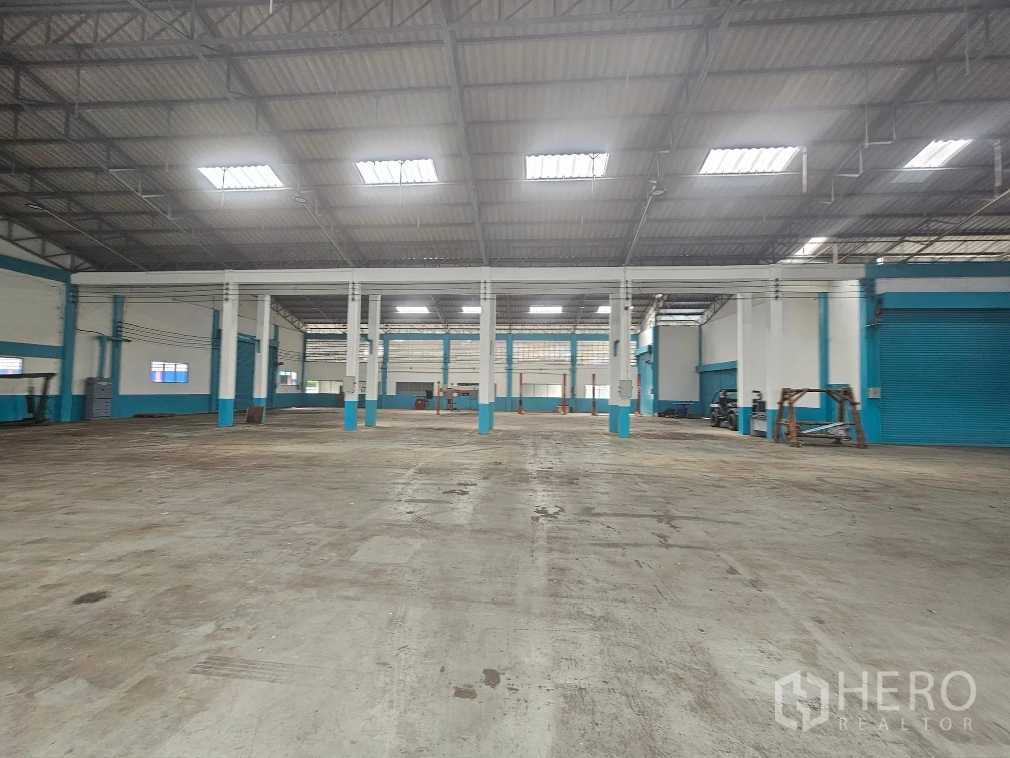 Factory for rent or sale in Mueang Rayong, Rayong - Expansive warehouse hall with multiple bays, roller shutter doors, skylights and reinforced concrete flooring.