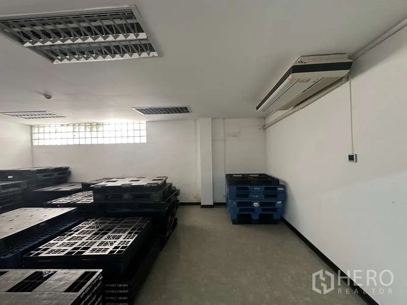 Warehouse for rent in Khlong Sam Wa, Bangkok - Storage room with stacked plastic pallets and wall‑mounted air conditioner.