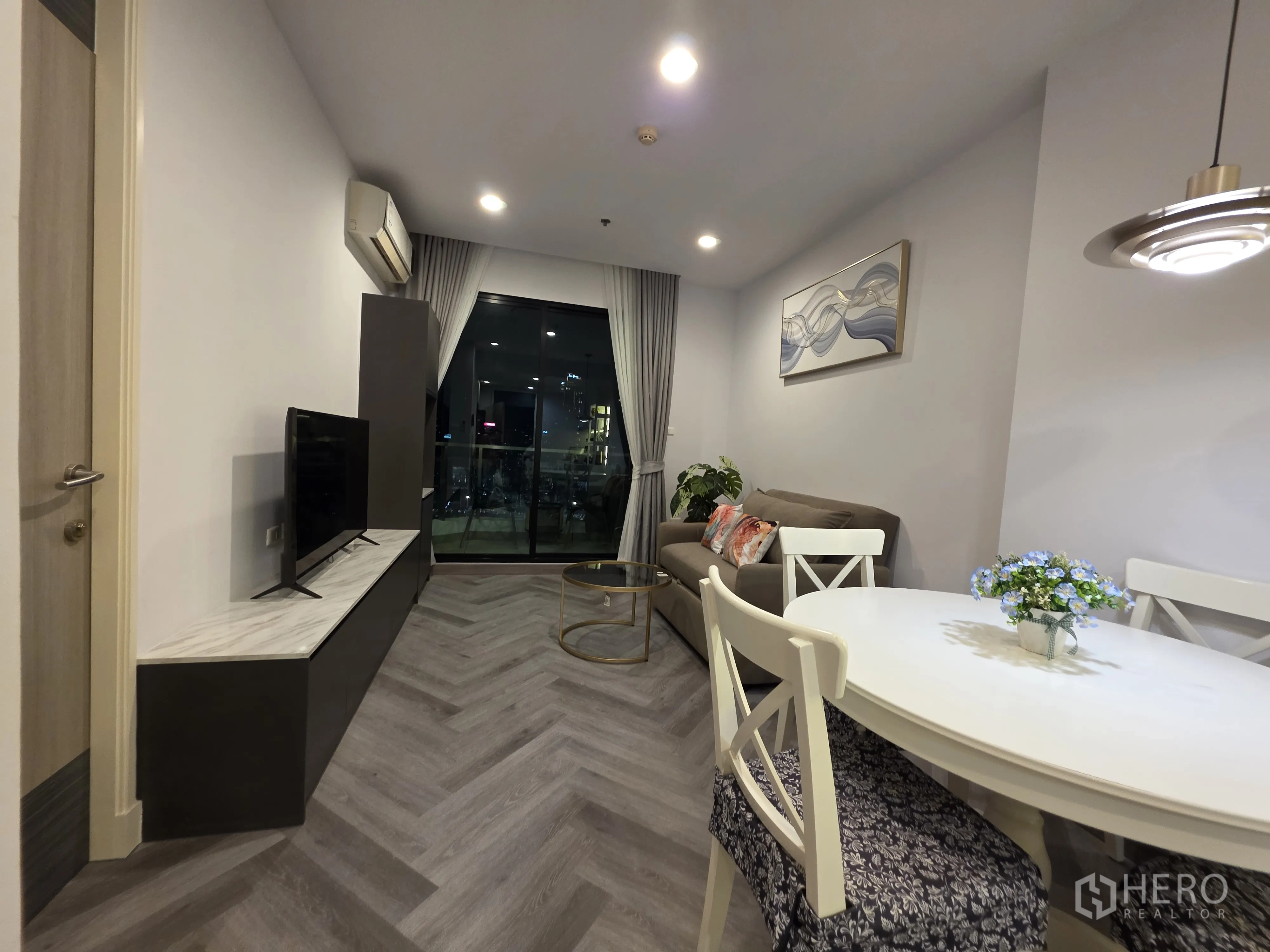 Condominium for rent in Bang Kapi, Bangkok - Open-plan living and dining area with TV, round table, and balcony access.