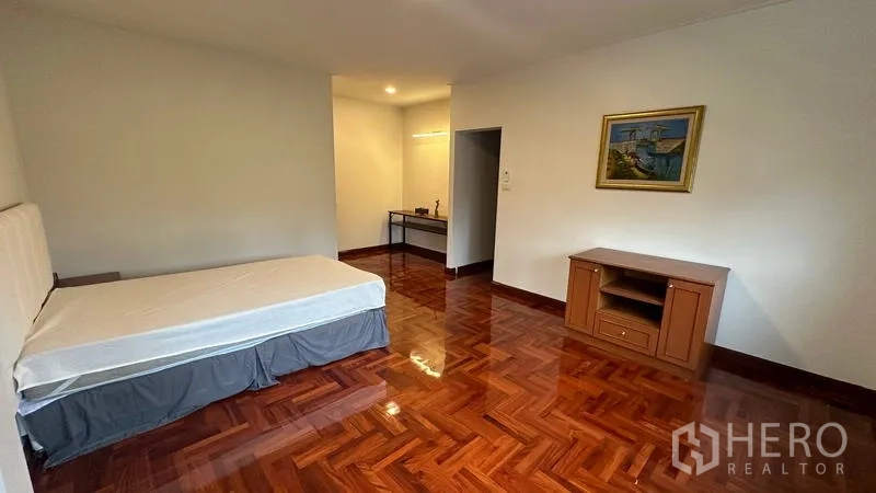 Detached House for rent in Watthana, Bangkok - Bright bedroom with bed, desk nook and wooden flooring.