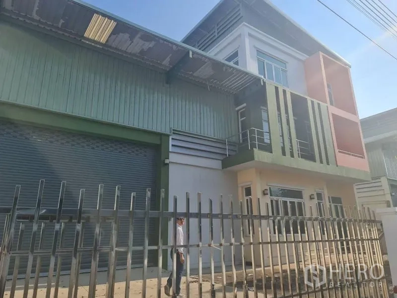 Factory for rent or sale in Lam Luk Ka, Pathum Thani - Street-facing facade with security fence, office balconies and loading door.
