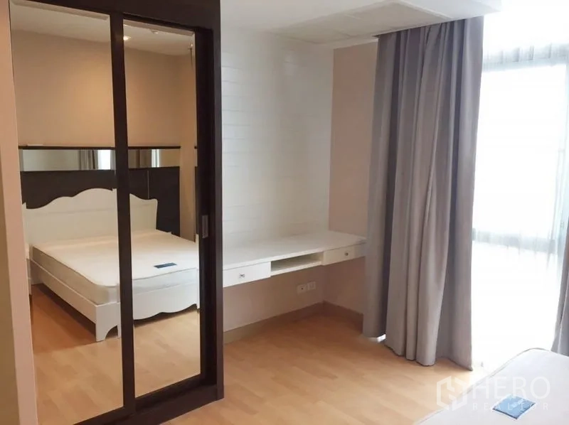 Condominium for rent in Khlong Toei, Bangkok - Bedroom with sliding mirrored closet, study desk, and window drapes.