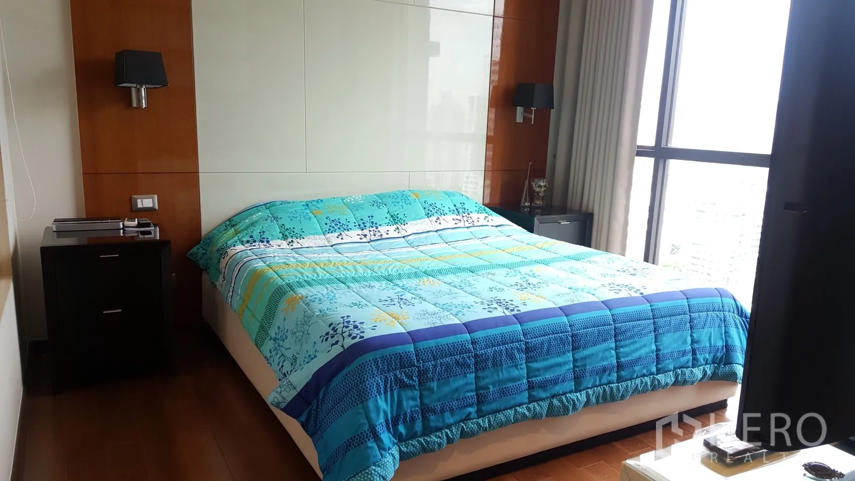 Condominium for rent or sale in Khlong Toei, Bangkok - Master bedroom with floor-to-ceiling window, wood panel accents and a double bed dressed in a blue duvet.