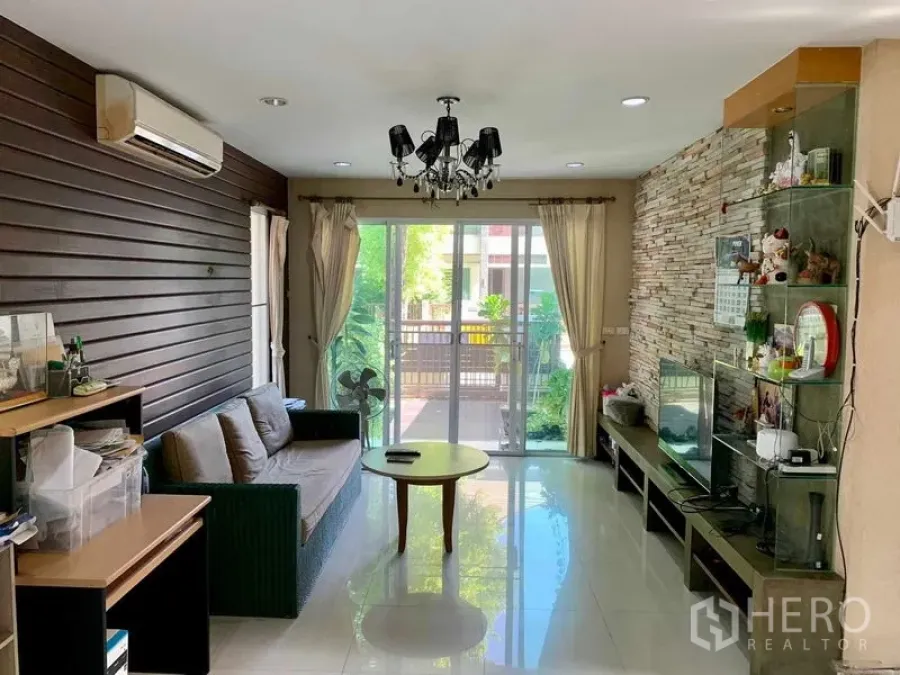 Detached House for rent in Prawet, Bangkok - Living room with sliding glass doors to a terrace and a stone feature wall.