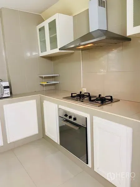 Detached House for rent in Watthana, Bangkok - Modern L-shaped kitchen with gas hob, oven, range hood and white cabinets.