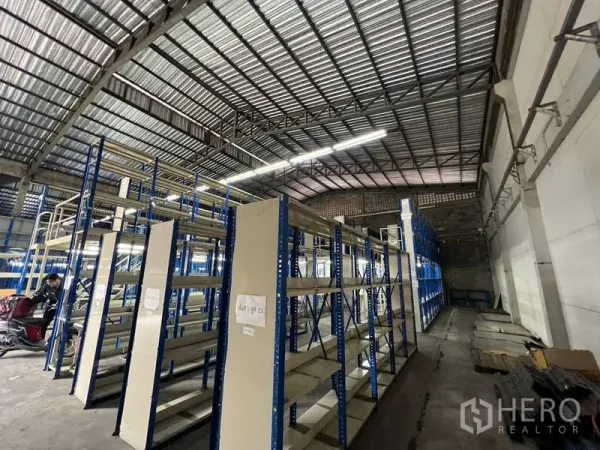 Warehouse for rent in Khlong Toei, Bangkok - Aisles of heavy-duty shelving under a tall corrugated roof with open loading space along the wall.