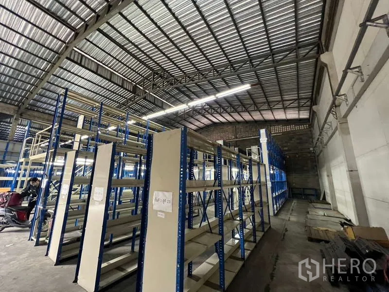 Warehouse for rent in Khlong Toei, Bangkok - Aisles of heavy-duty shelving under a tall corrugated roof with open loading space along the wall.