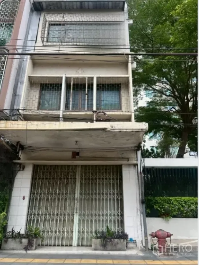 Shophouse for sale - Multi-storey shophouse facade with folding metal gates, small balcony, and street-side planters in Khlong Toei, Bangkok.