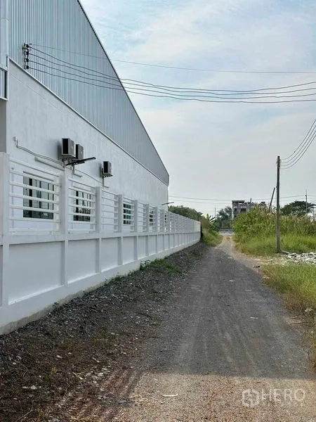 Warehouse for sale in Khlong Luang, Pathum Thani - Exterior side of the warehouse with windows, AC units and boundary wall by an access road.