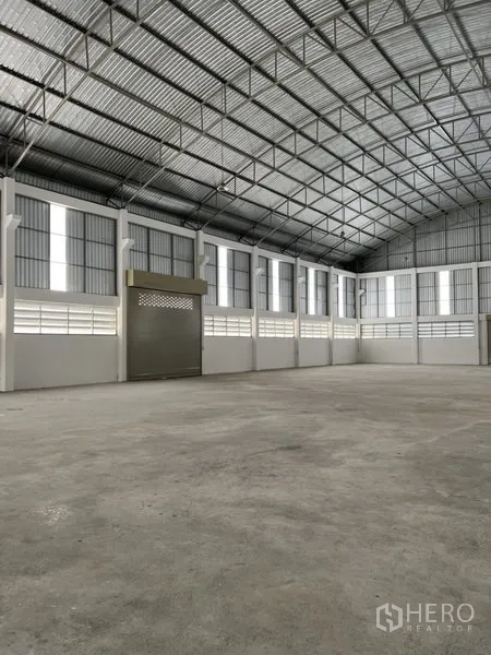 Factory for rent or sale in Bang Bo, Samut Prakan - Open concrete production floor with high-clear ceiling and a corner roller shutter.