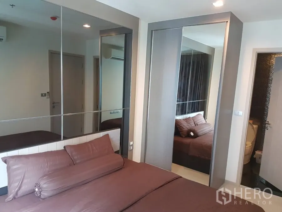 Condominium for rent in Khlong Toei, Bangkok - Cozy bedroom with brown bedding, mirrored wall panels and a sliding wardrobe.