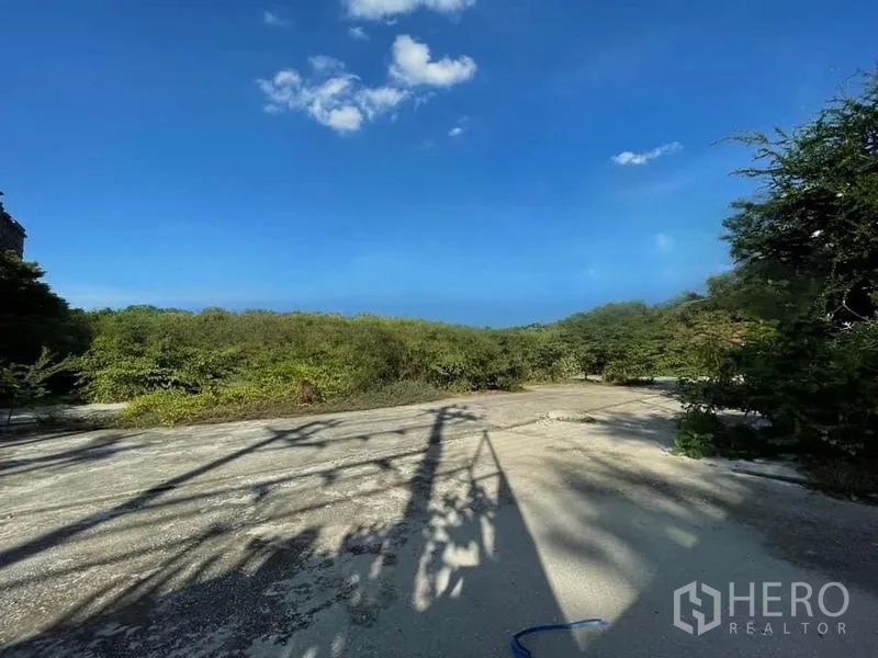 Land for rent in Phra Khanong, Bangkok - Level plot with hardstand surface, surrounding bushes, and power line shadows in the Phra Khanong area.