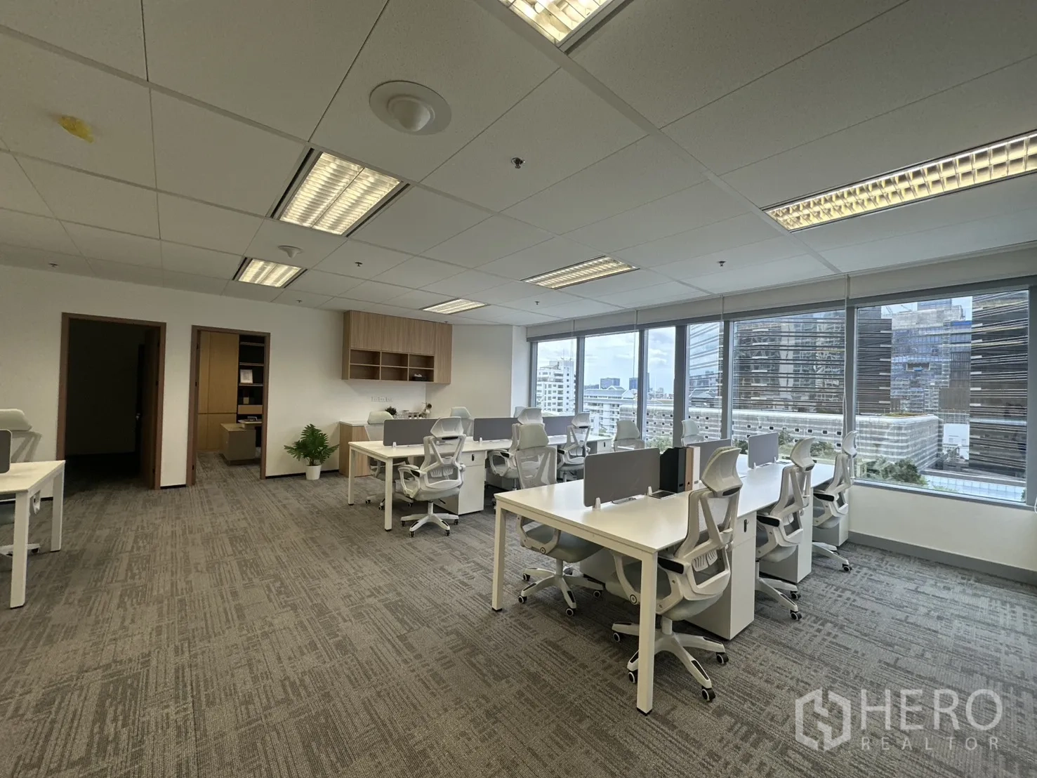 Office Space for rent in Pathum Wan, Bangkok - Work area beside wide windows overlooking city buildings and trees.