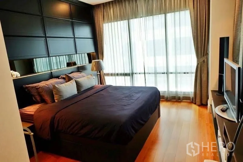 Condominium for rent in Khlong Toei, Bangkok - Master bedroom with dark feature wall, king bed, hardwood floor and full-height windows with sheer curtains.